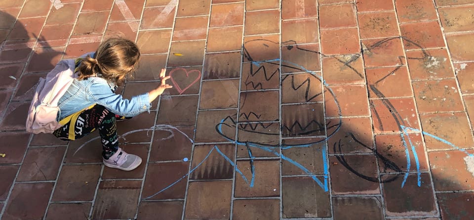 Little girl drawing chalk shapes outside, including a shark and a heart.