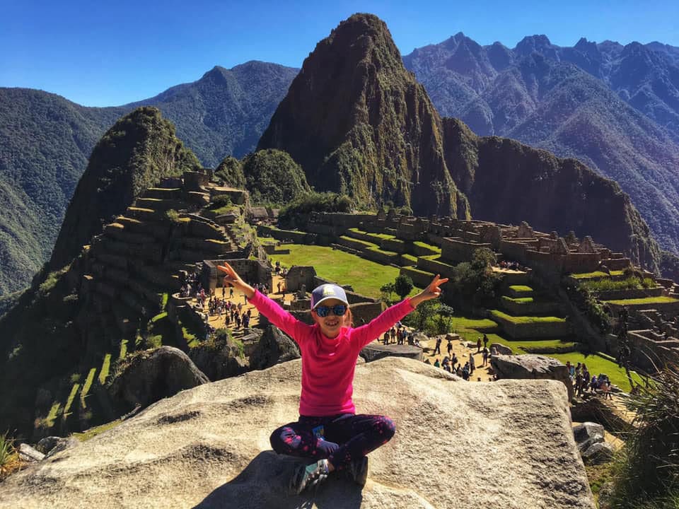 Little girl posing on top of the mountain in Machu Picchu, a must stop on our Peru family vacation itinerary.