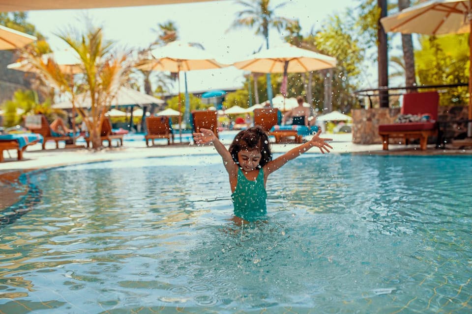 A young girl in a teal swim suit splashing while enjoy one of the many pools at the JA Palm Tree Court.