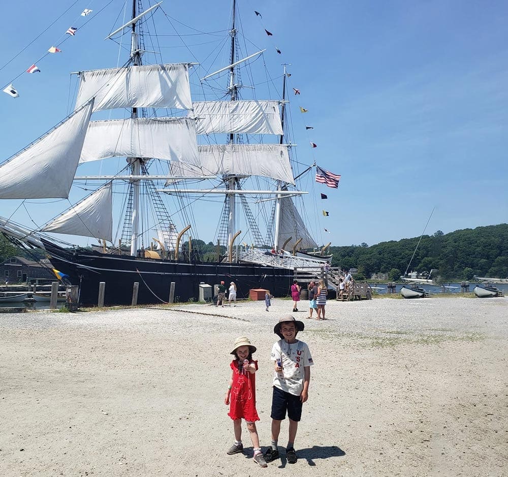 Boy and girl in front of a big boat at The Mystic Seaport Museum, one of the best things to do in Mystic with kids.