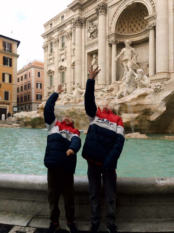 Two young boys throwing coins in the Trevi Fountain in Rome.