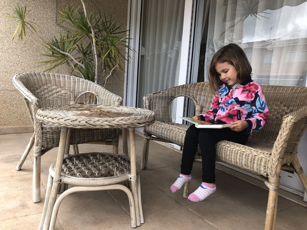 Little girl reading a book on an outside patio.
