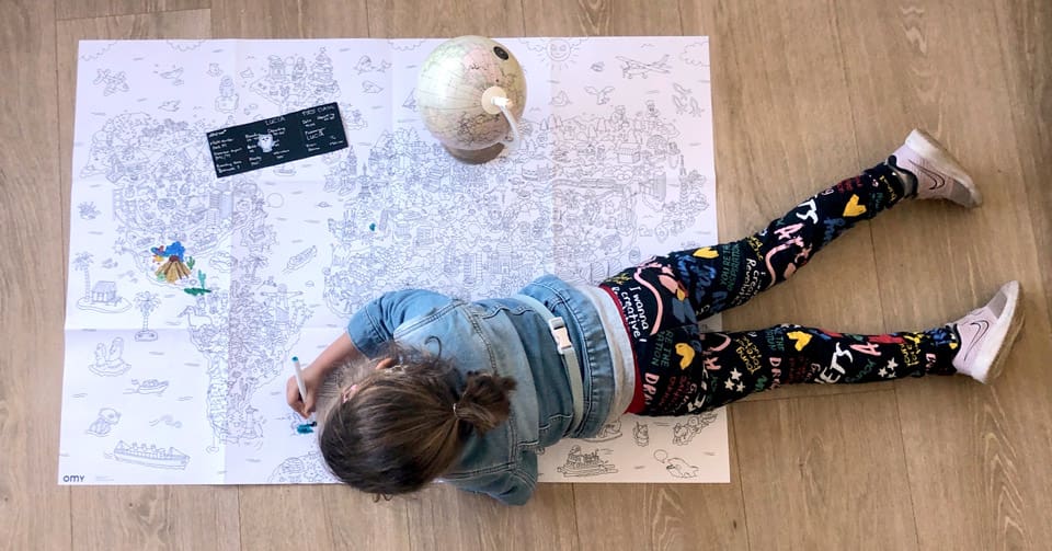 Girl lays on the floor coloring a large map.