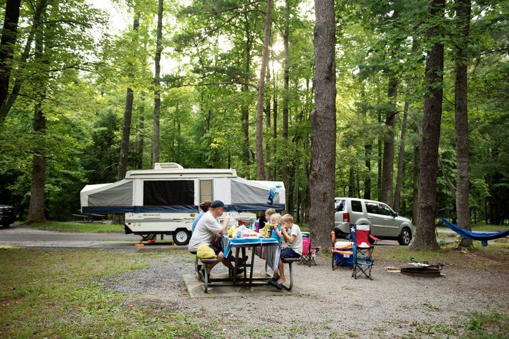 Family eating a meal on a bench outside of their RV pop-up trailer, one of the best affordable summer vacation ideas in the United States with kids.