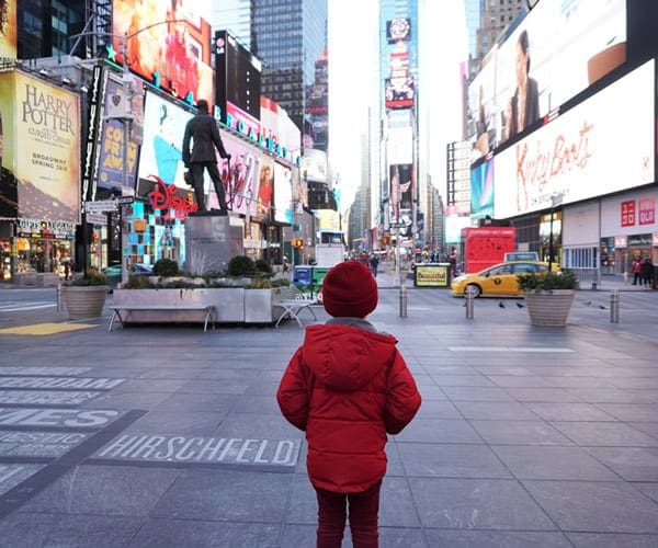 A child, wearing red, stands in Times Square in New York City looking at all the bright lights.