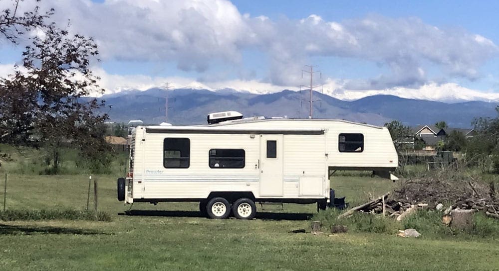 5th-wheel RV stationed on the grass with mountains in the background. One of the recommendations for RV safe travel.