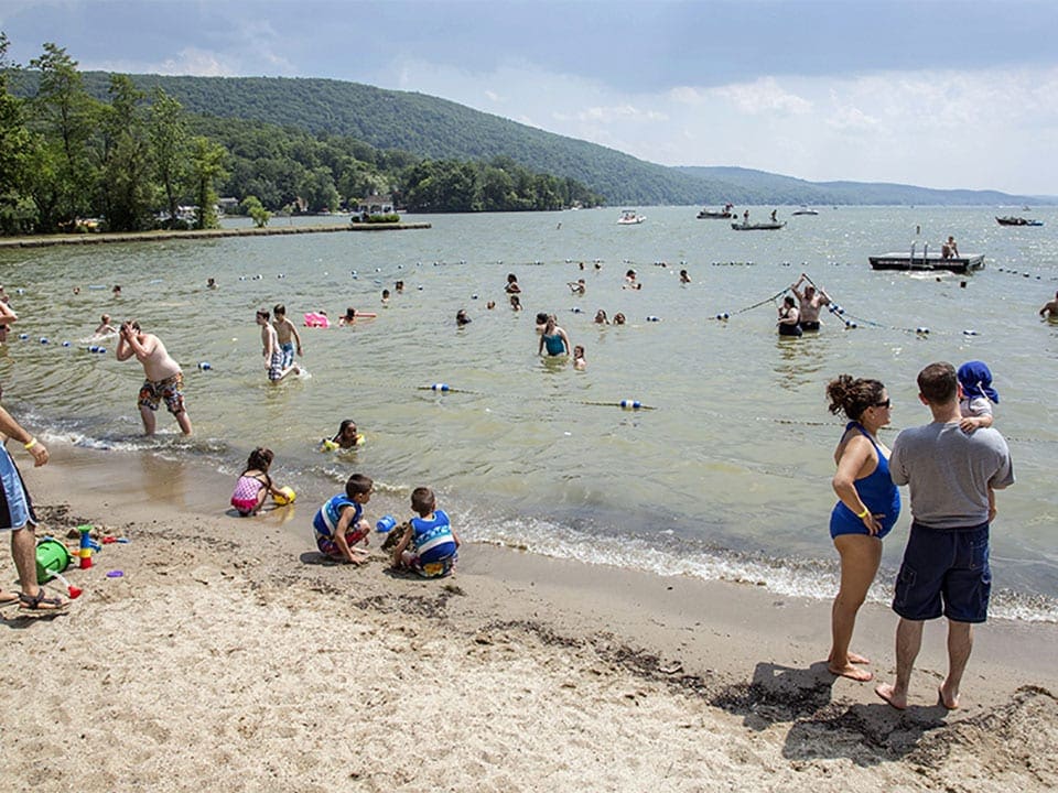 People playing in the sand and water along the shore of Greenwood Lake, one of the best lakes for a family vacation within 4 hours of NYC.