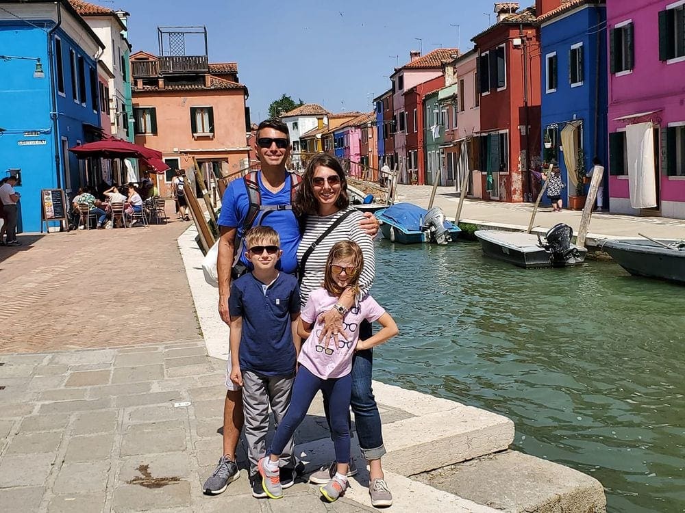 Family of four stands along the canal in colorful Burano, Italy, one of the Best Colorful Towns for families.