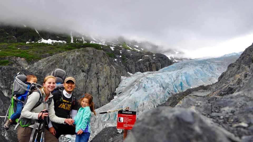 Family of four stands in front of a glacier at the Kenai Fjord National Park, one of the best places for families in the U.S.