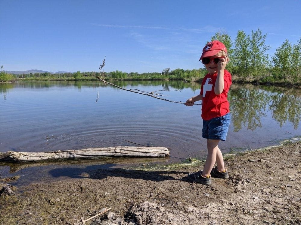Small boy stands near a lake while hiking near Denver.