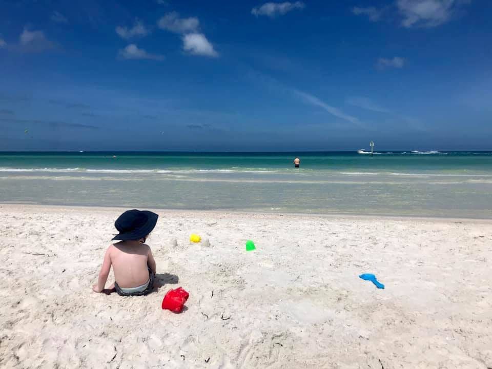 Little boy with blue hat sitting on beach surrounded by toys in Clearwater Beach in Florida