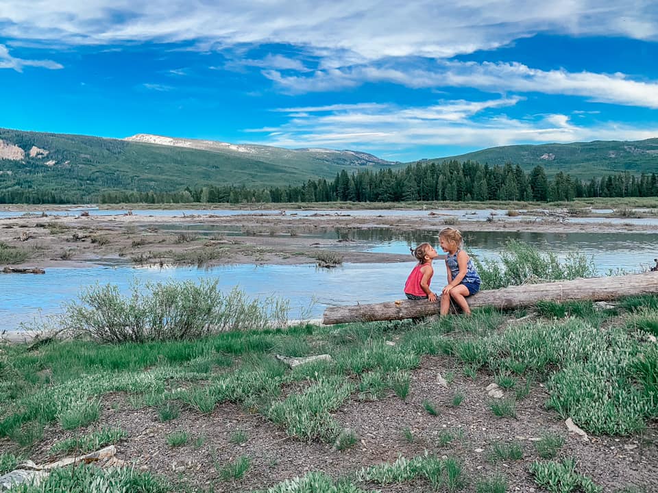 Two small girls sit on a long near a small pond in the Grand Tetons.