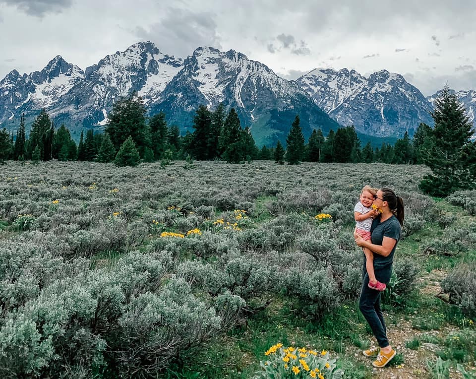 Mother and daughter stand in a field of flowers in front of mountains in the Grand Tetons, one of the best cool-weather destinations in the United States for families.