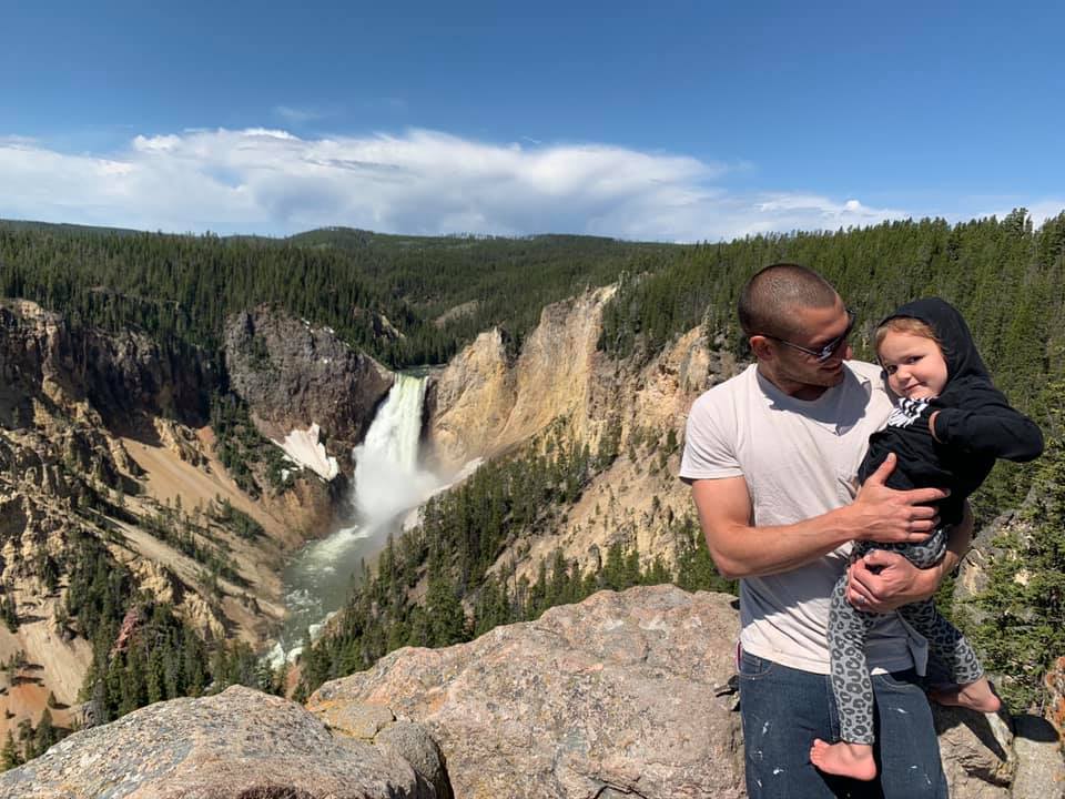 Father and daughter stand above a large waterfall in Yellowstone National Park, one of the best places for families in the U.S.