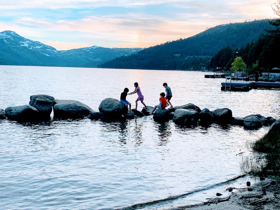 Four kids play along a series of large rocks in the water on Lake Tahoe.