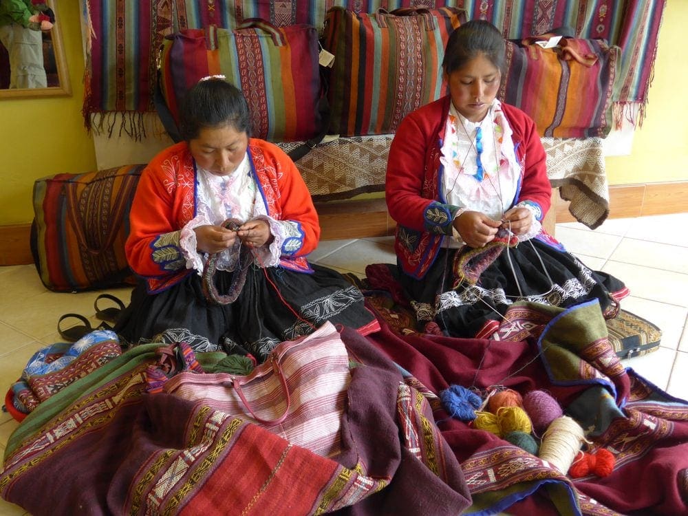 Two Peruvian women sit knitting within a shop at a market in the Sacred Valley, Peru.