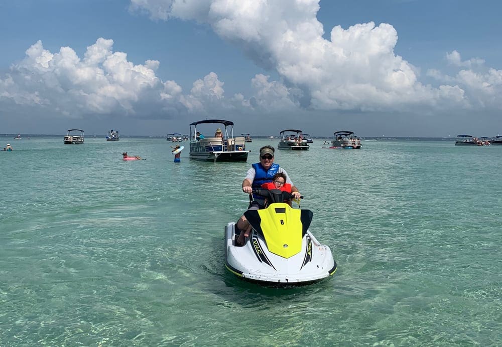 Father and son ride a jet ski off the coast of one of the best Florida beaches for families, Destin Beach.