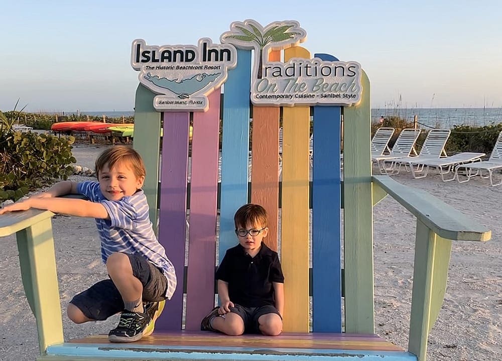 Two boys sitting on large colorful oversized outdoor wooden chair on beach in Sanibel Island in Florida