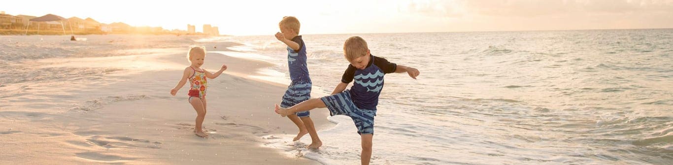 Two boys and a girl playing on sand near ocean at Navarre Beach, one of the best Florida beaches for families.