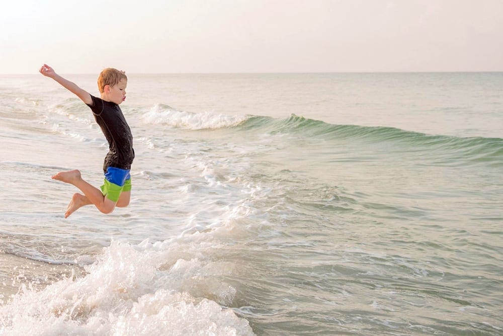 Young boy jumping over a wave in the ocean in Panama City Carillion Beach in Florida