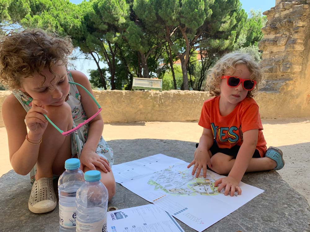 How to prepare kids for a trip, having them review maps and navigate short walks while traveling is a wonderful option. Here, two kids look at a map in Lisbon at St. Georges Castle.