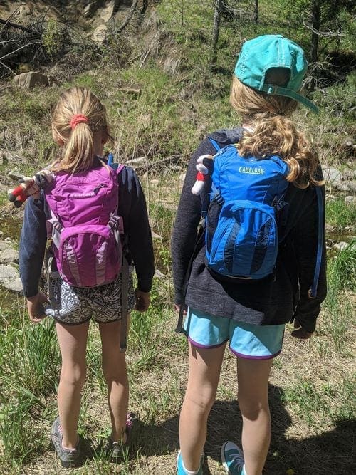 Two young girls stand with their packpacks preparing to hike near Denver.