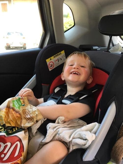 Young boy in a car seat enjoys a quick snack.