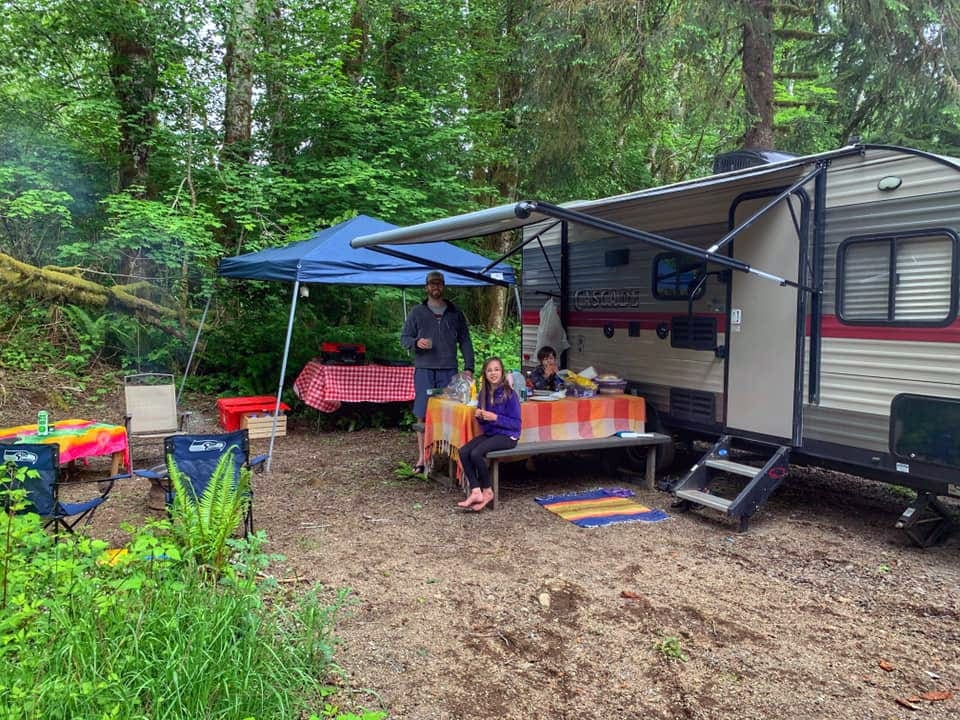 Family enjoying a meal at a camp site under a canopy of their RV.