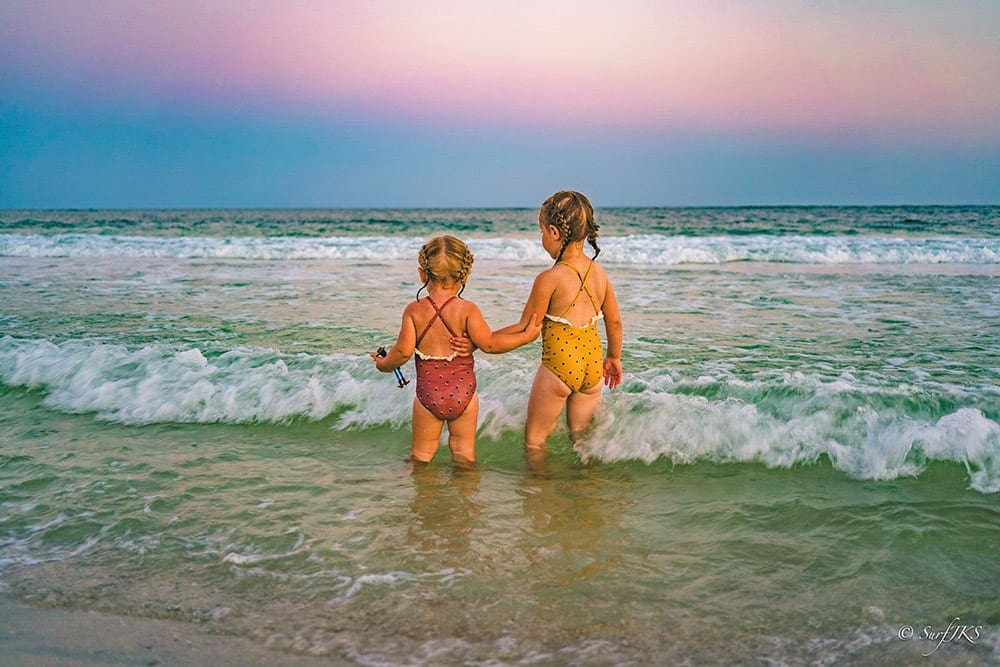 Two little girls with french braids standing in ocean off Pensacola Beach, one of the best Florida beaches for families.
