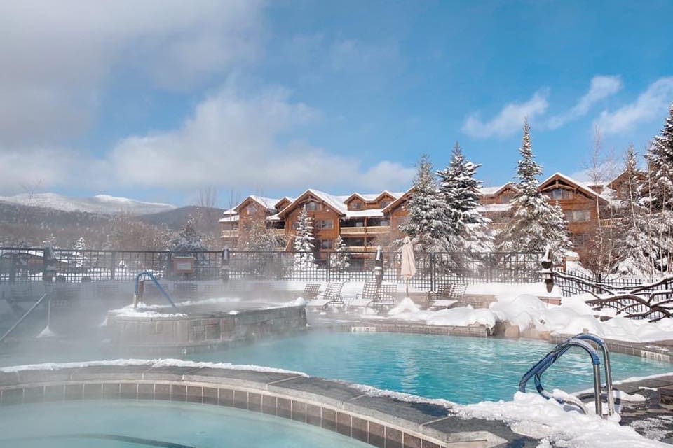 The outdoor heated pool and hot tub at the Whiteface Lodge on a winter day, with snow around the edge of the pool area.