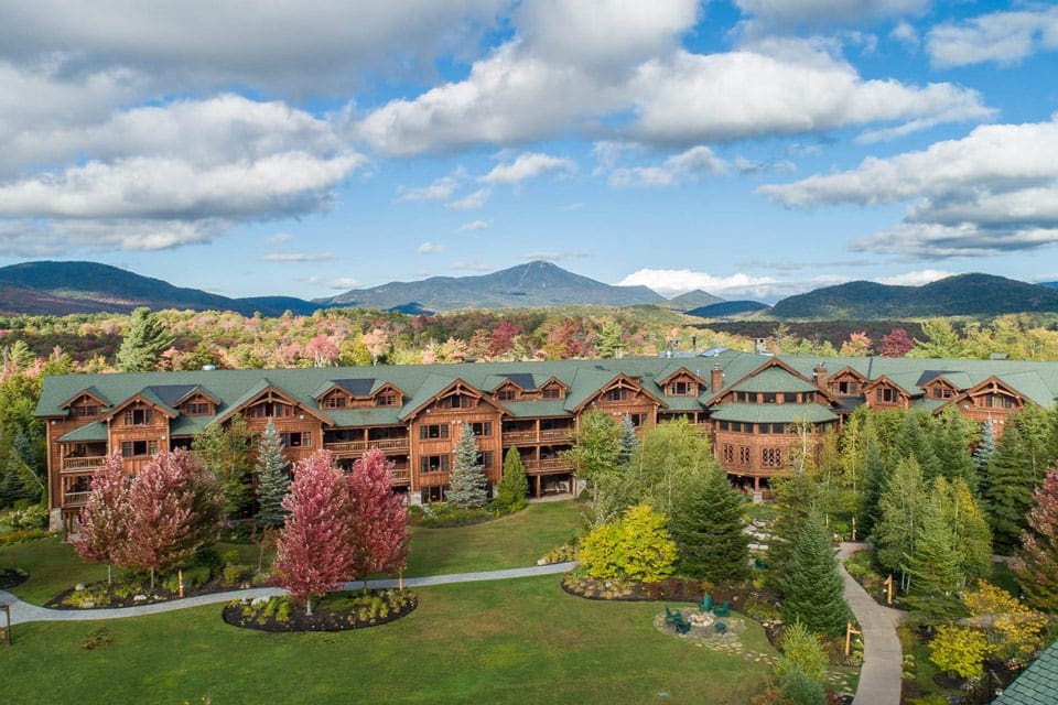 An aerial view of Whiteface Lodge, one of the best summer lake resorts in the Northeast for families, nestled among vibrant trees with mountains in the distance.