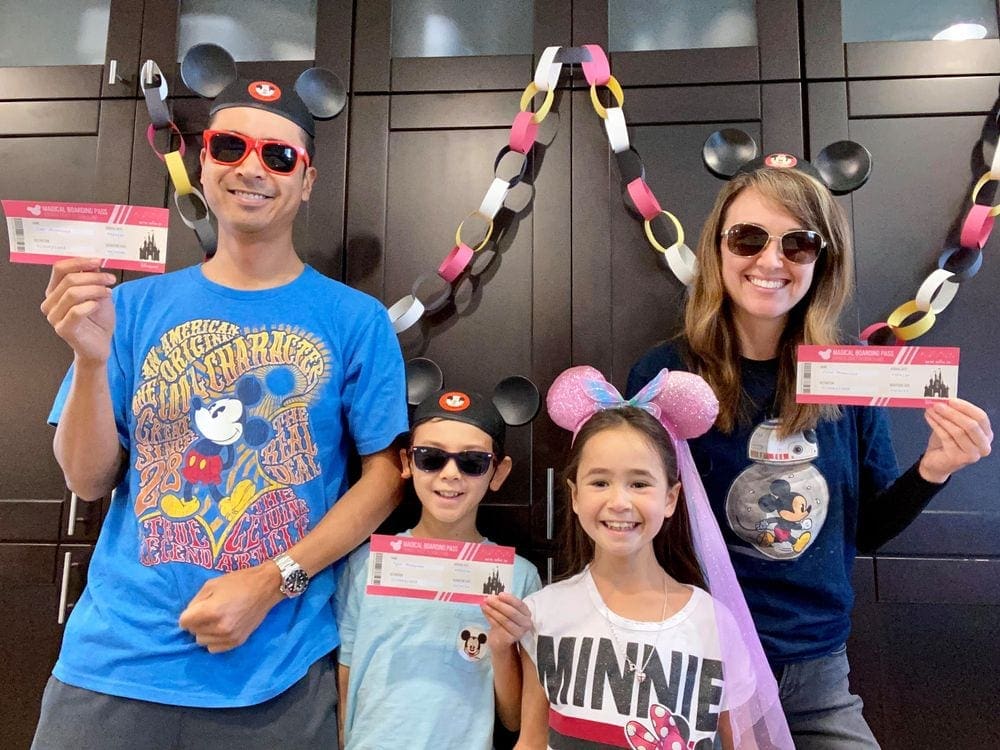 Family of four stands amongst Disney decorations as they prepare to have a Disney theme night at home. A theme night is a great family staycation idea!