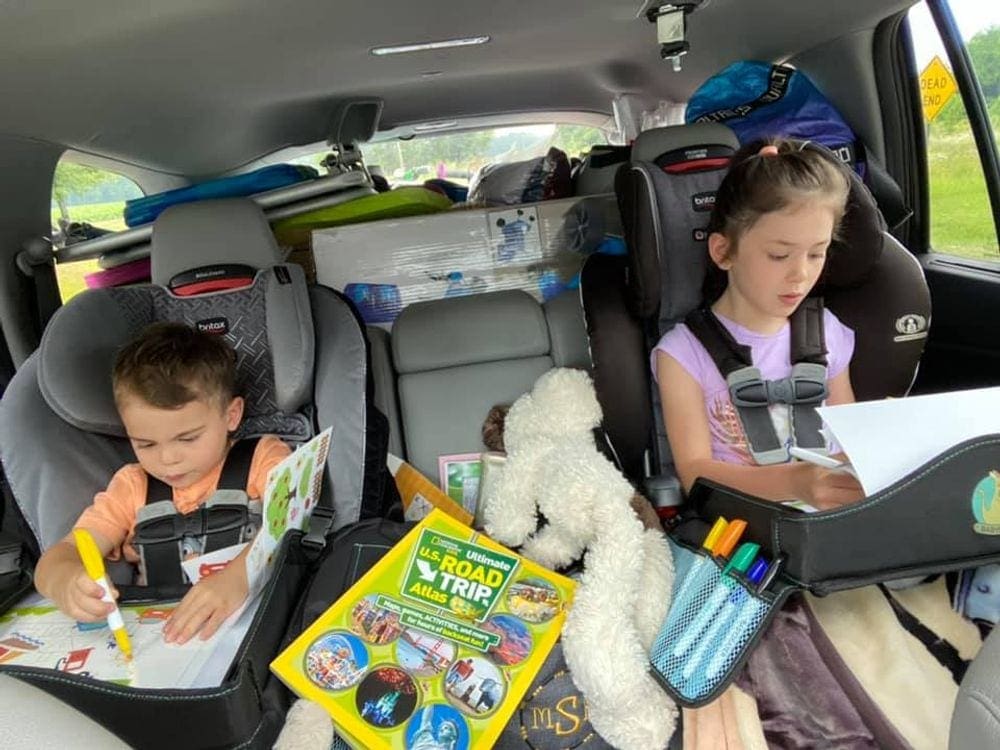 Two kids sit in their car seats when traveling, while coloring in the back seat.