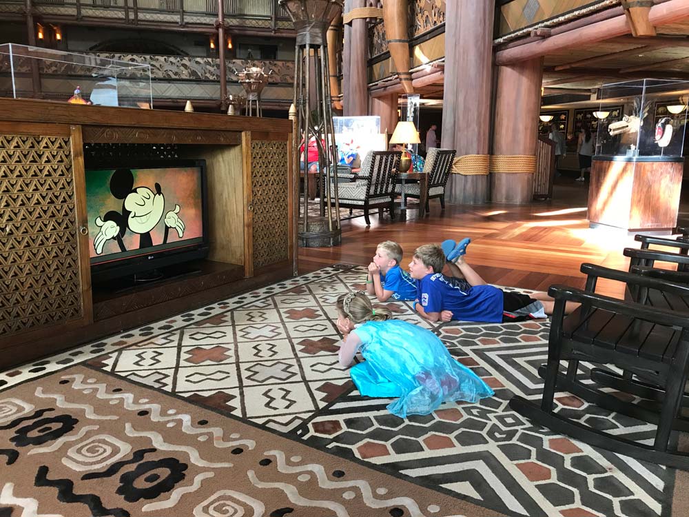 Three children laying on carpet watching Mickey Mouse on TV