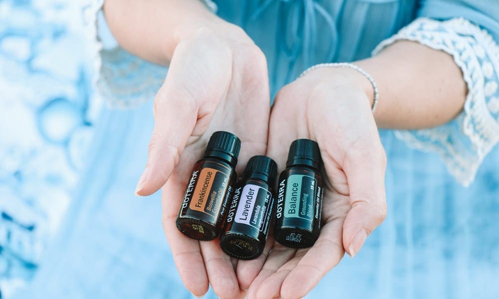 White hands holding three bottles of doTerra essential oils: Frankincense, Lavendar, and Balance.