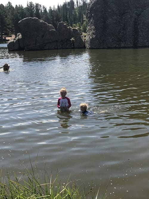 Two young kids swim in the water with large boulders in the background at Custer State Park.