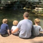 Dad with 2 little kids sitting on the side of the river