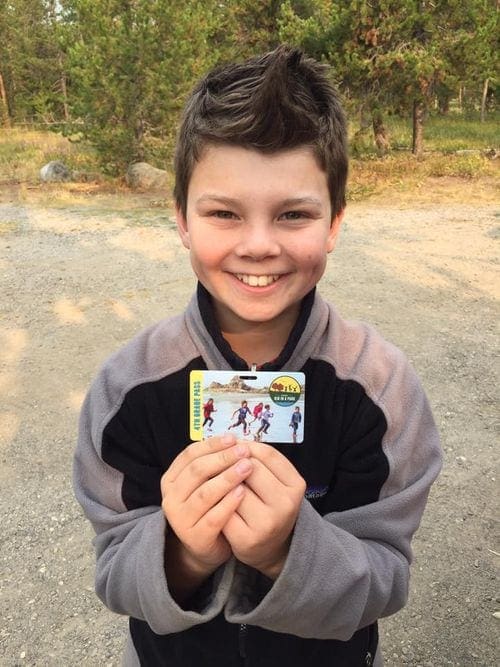 A 4th grade boy smiles while holding his Every Kid Outdoors national park pass.