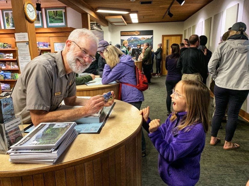 A 4th grade girl excitedly accepts her park pass from a smiling park ranger.