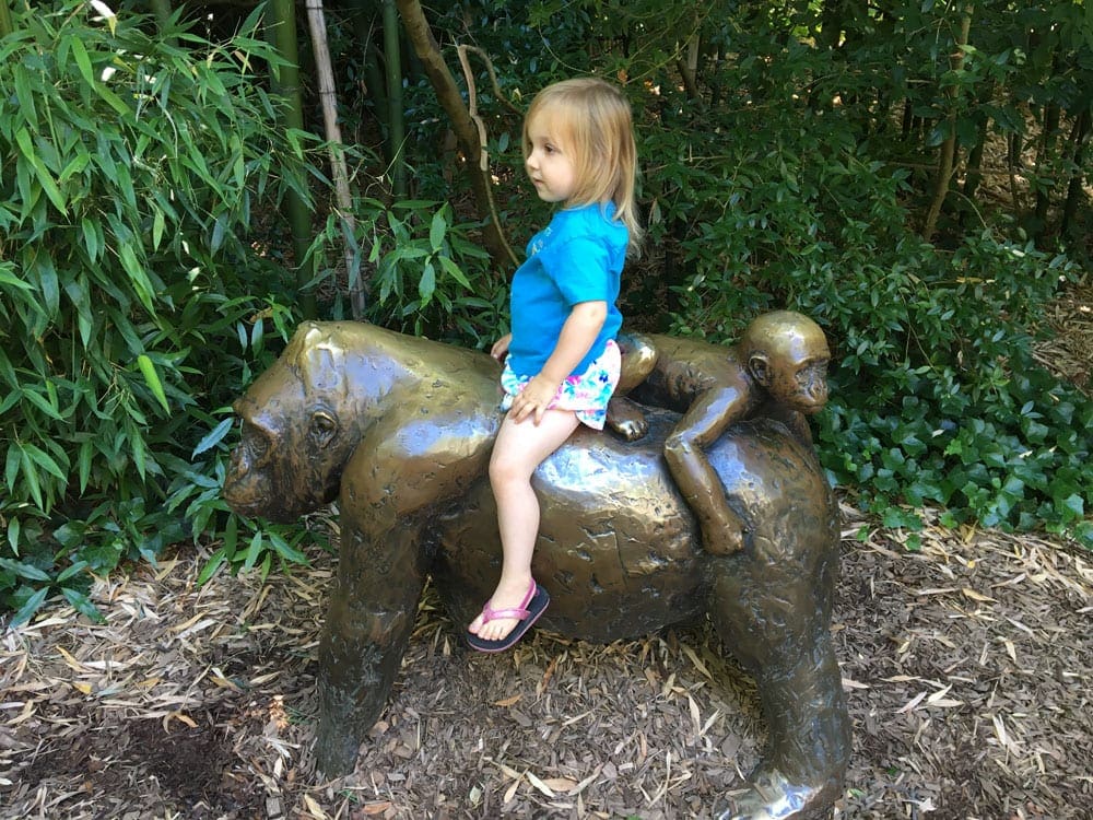 Girl sits on a gorilla statue at the Woodland Park Zoo.