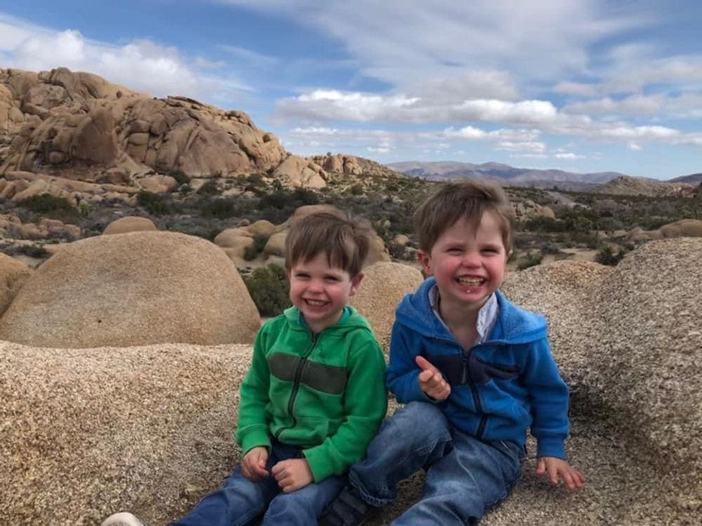 Two young boys sit laughing in Joshua Tree National Park, one of the best west coast national parks for kids!