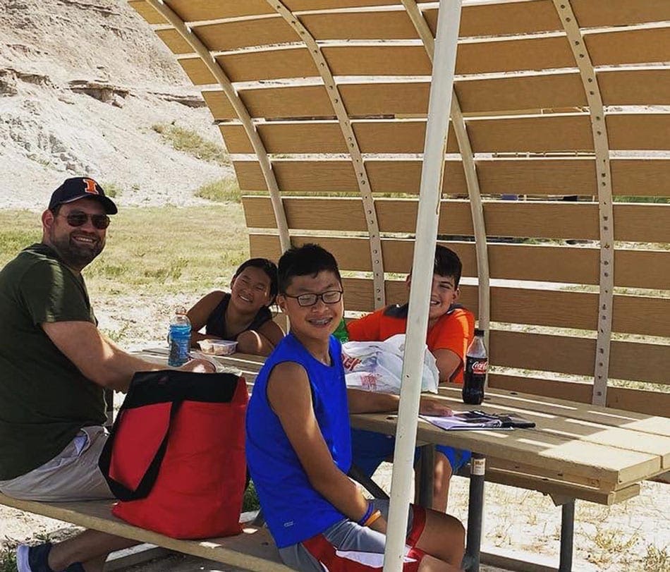 Family of four picnics while on a stop during a roadtrip. Picnics are a favorite on our list of Coronavirus Travel Tips For Families.