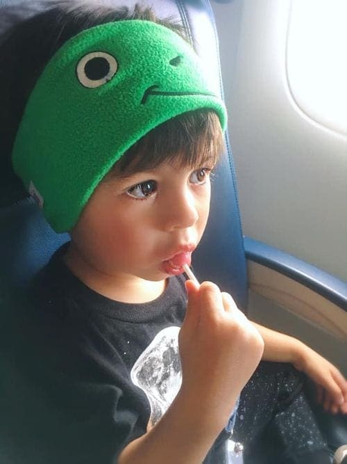 Small boy wearing headphones on a plane enjoys a sucker.