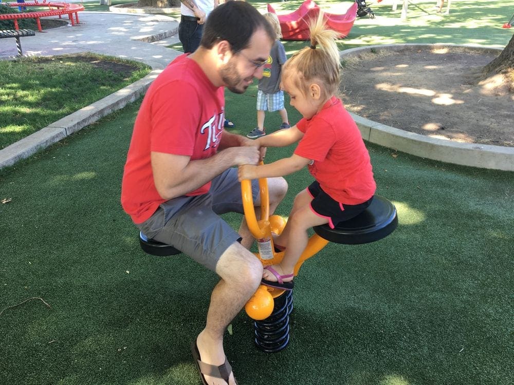 Father and daughter enjoy a small teeter totter at a park. Letting kids help plan the itinerary is a great way of keeping kids entertained on a trip.