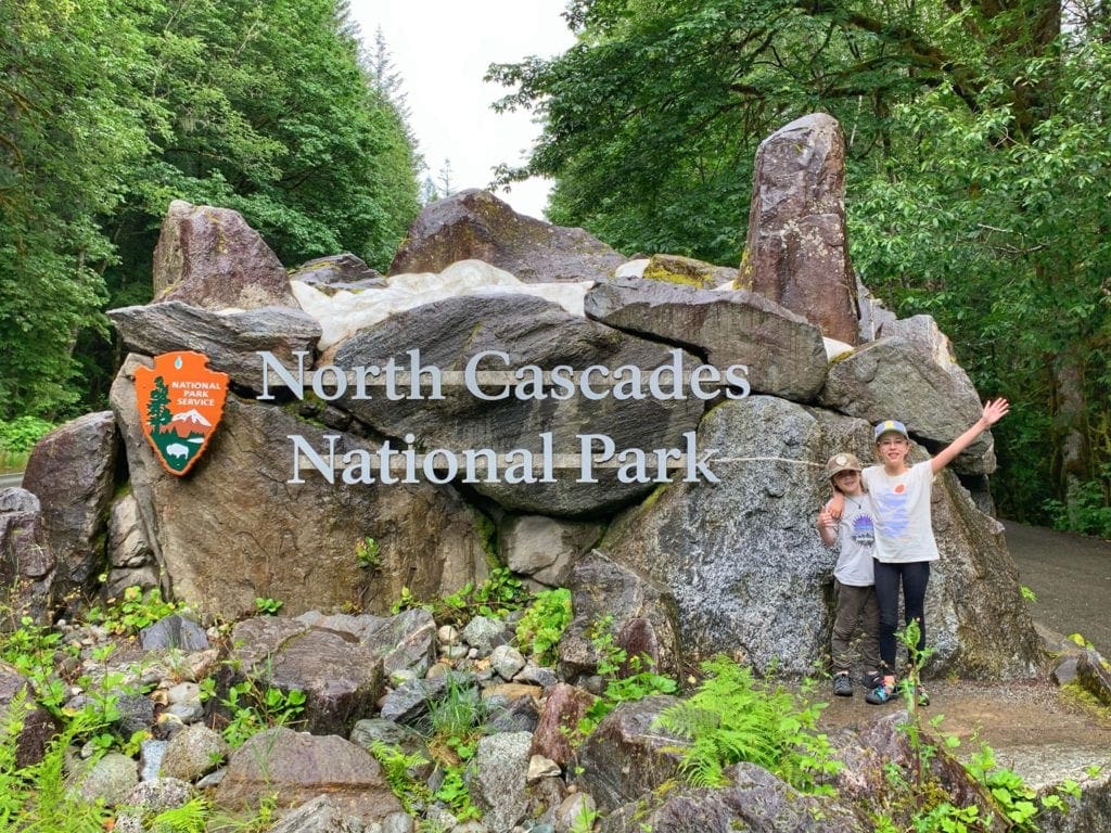 Two kids pose with the entrance sign to North Cascades National Park.