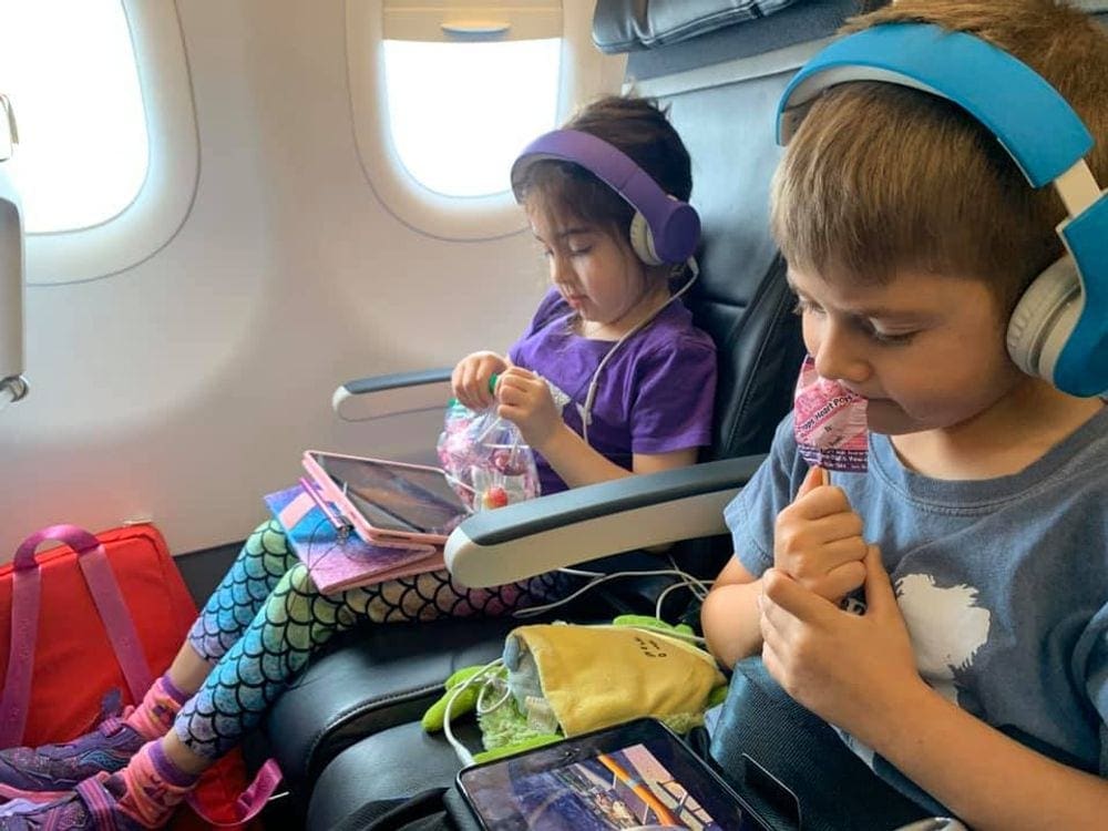 Two young kids enjoy suckers on an airplane, snacks are one of our tips for keeping kids entertained on a family trip.