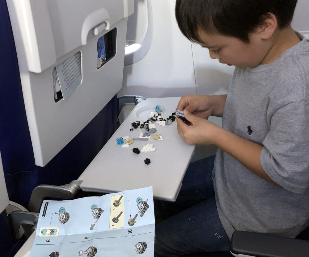 Small boy playing with legos on an airplane, new toys are one of our tips for keeping kids entertained on a family trip.