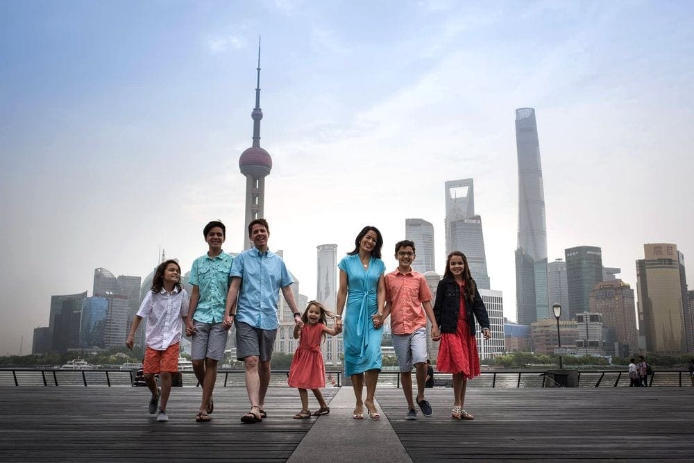 A family of seven holds hands while walking in front of the Shanghai skyline.