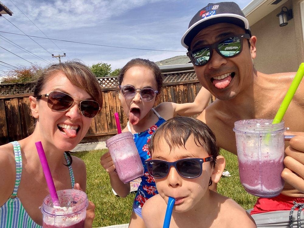 Family of four makes silly faces while enjoying pink homemade smoothies.