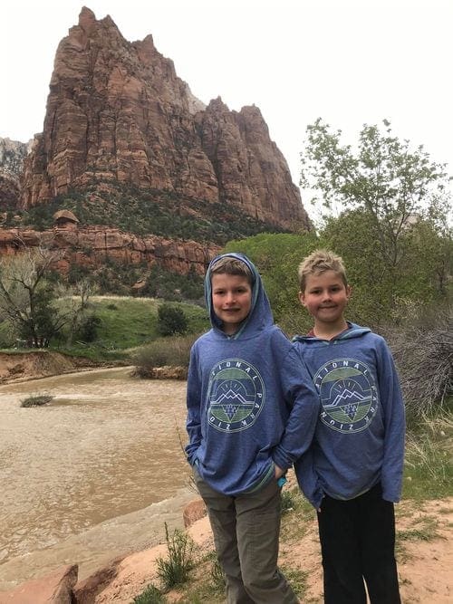 Two boys stand in front of a large rock formation in Zion National Park.